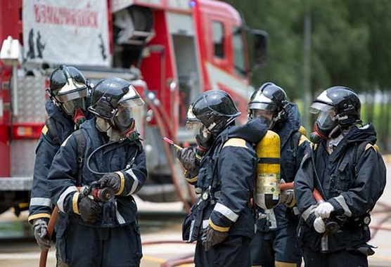 Firefighters in full gear with fire trucks in the background