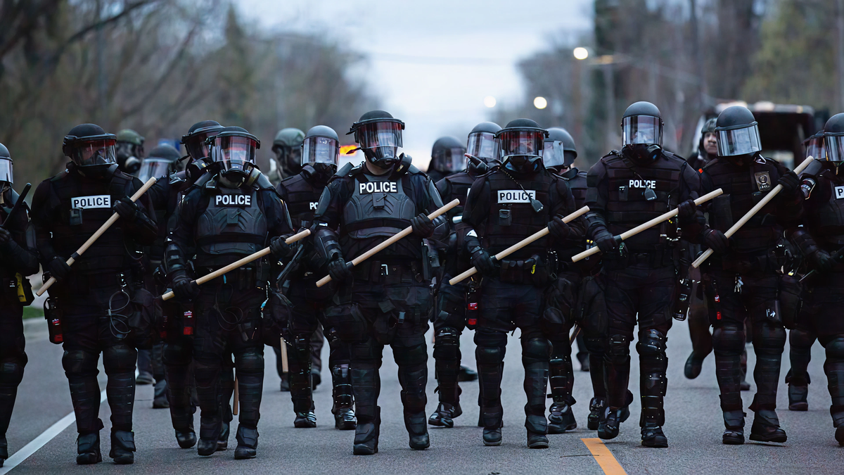 Line of police officers in riot gear with batons on a street